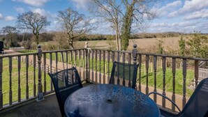 An outdoor patio with a table and chairs, a wooden fence, and a view of a field and trees. - 3 Bed in Dereham (oc-65903) (Foulsham)