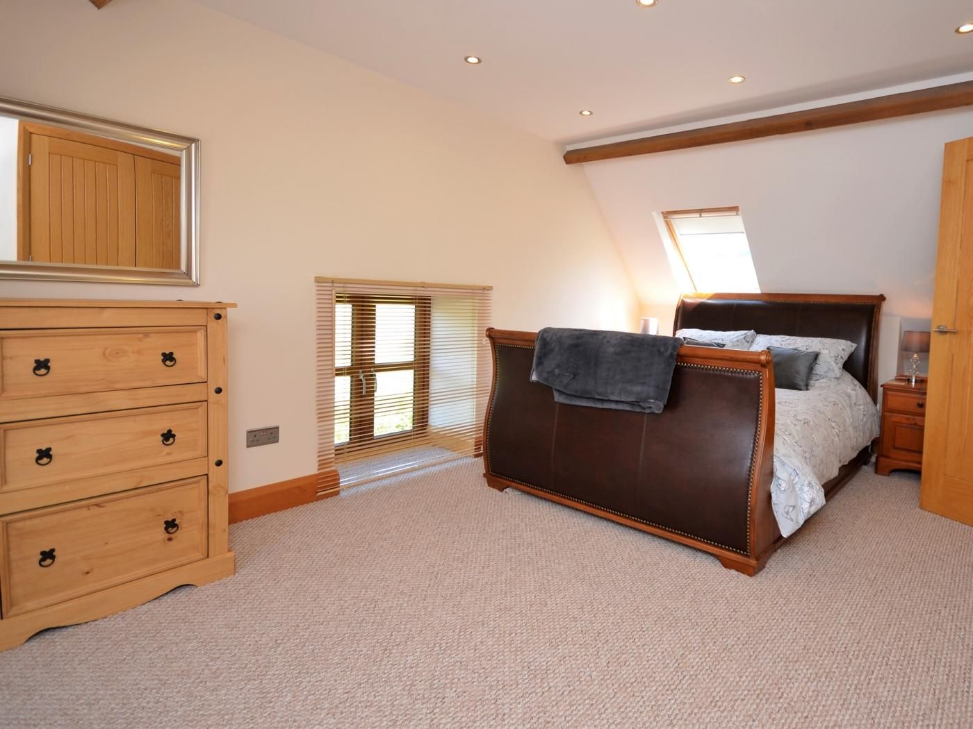 A bedroom with a wooden dresser, a bed with a dark headboard, a nightstand, and a window with blinds.