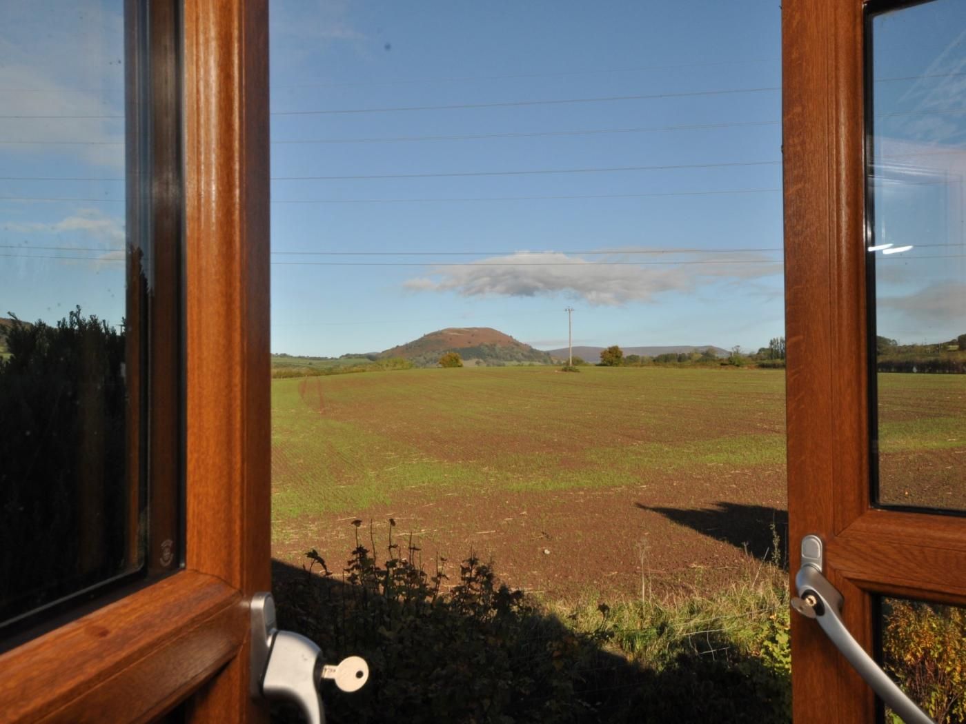 A view through a window with a door, overlooking a field with a hill in the distance.