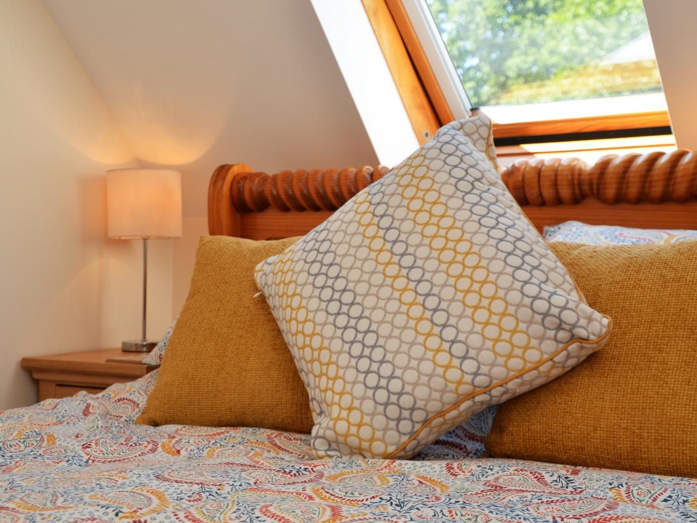 Ein Schlafzimmer mit einem Bett, einem Nachttisch, einer Lampe und einem Fenster mit Blick auf Grünflächen.