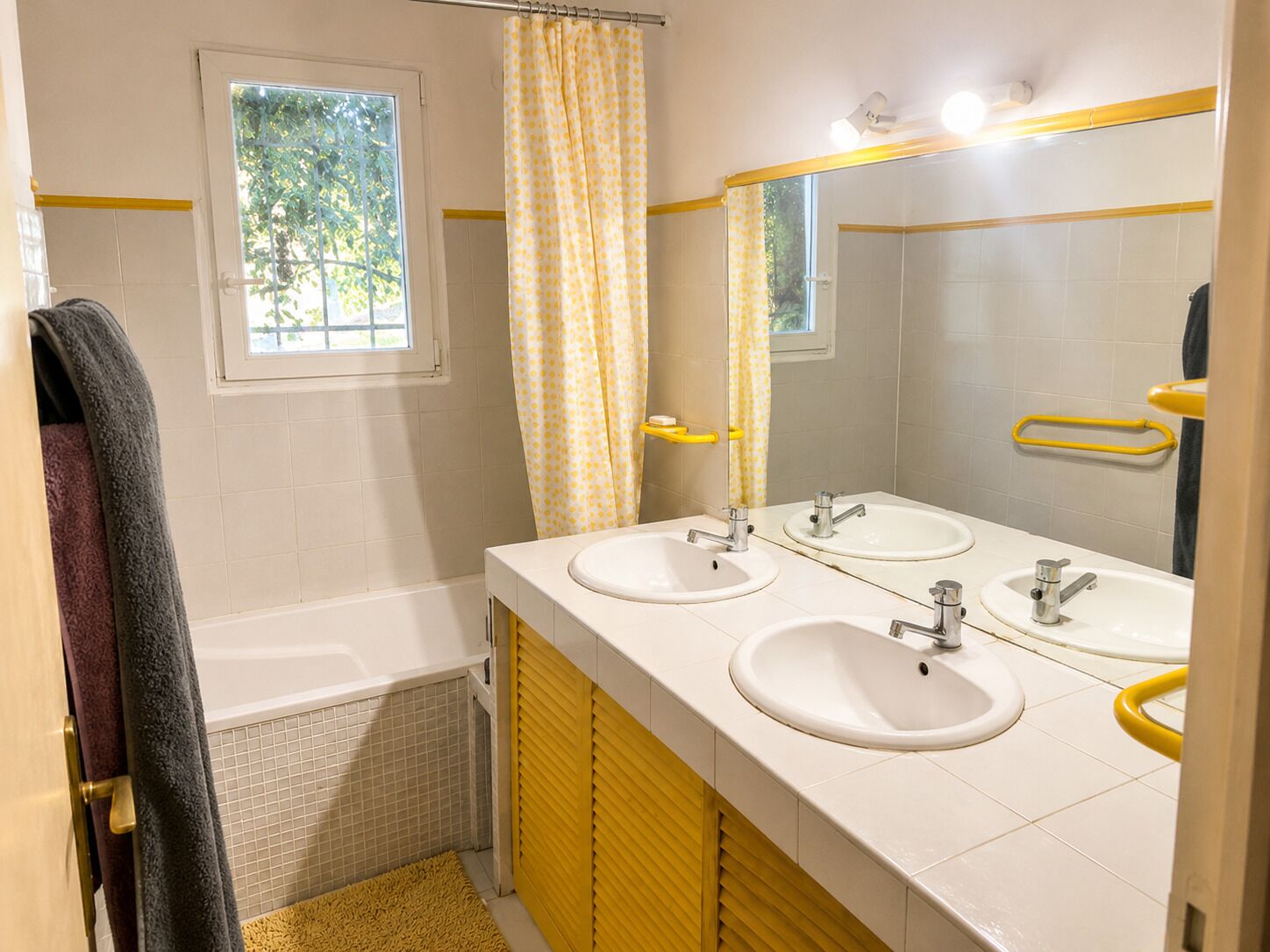 Un baño con dos lavamanos, una bañera, un ventanal y un perchero amarillo.