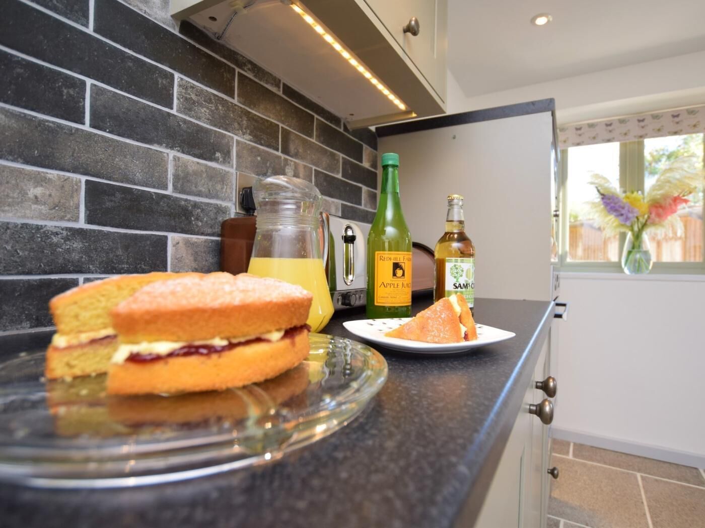 Una encimera de cocina con un sándwich, una jarra de jugo y dos botellas de licor.