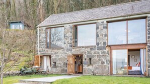 Une maison en pierre avec de grandes fenêtres, une porte en bois et une pelouse devant.