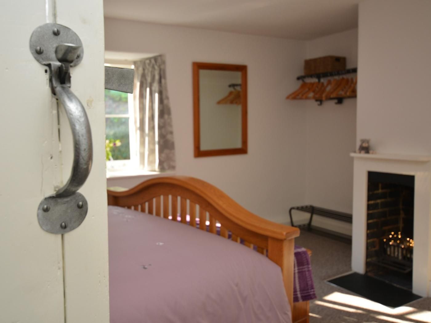 Ein Schlafzimmer mit Bett, Kamin, einem fenster mit Vorhängen und einem Spiegel an der Wand.