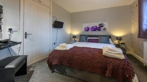 Un dormitorio con cama, mesitas de noche, televisor y escritorio.