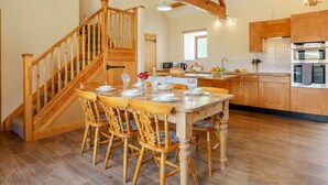 A dining area with a wooden staircase, a kitchen with wooden cabinets, and a dining table set for six. - 3 Bed in Middlesbrough (oc-72267) (Chop Gate)
