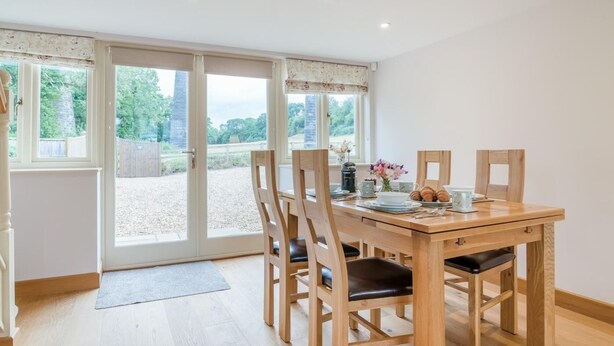 A dining area with a wooden table and chairs, a view through a glass door, and a small vase with flowers on the table. - 2 Bed in Bristol (oc-72582) (Winford)