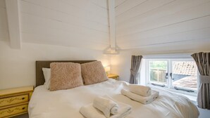 A neatly made bed with pillows, a bedside table, and a window with curtains. - 6 Bed in Norwich (oc-72652) (Hoveton)
