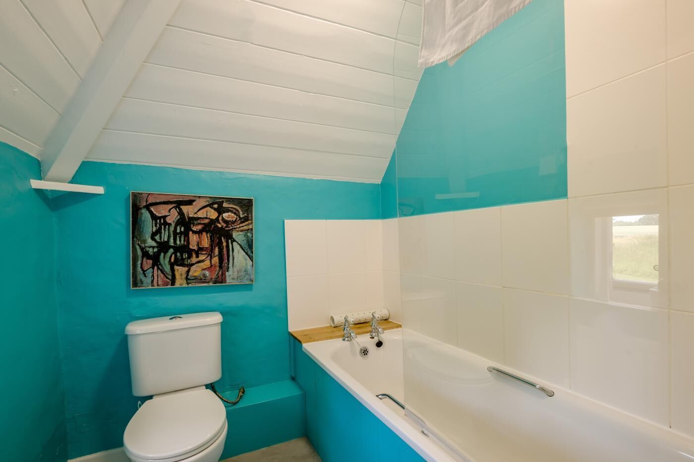 A bathroom with a toilet, bathtub, and a wall-mounted abstract painting.