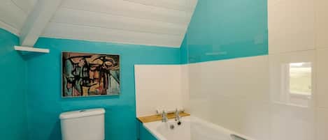 A bathroom with a toilet, bathtub, and a wall-mounted abstract painting.