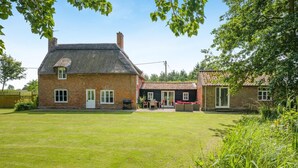 A brick house with a thatched roof, a fenced yard, and a patio area with outdoor furniture. - 6 Bed in Norwich (oc-72652) (Hoveton)
