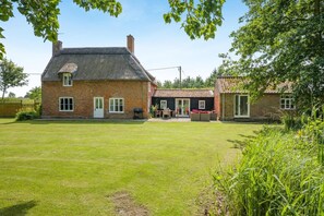 A brick house with a thatched roof, a fenced yard, and a patio area with outdoor furniture. - 6 Bed in Norwich (oc-72652) (Hoveton)