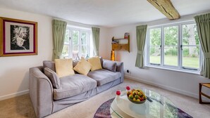 A living room with a grey sofa, a glass coffee table with fruit, and a painting on the wall. - 6 Bed in Norwich (oc-72652) (Hoveton)