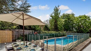 Área de piscina externa com mesa e cadeiras, um guarda-sol e cercado.