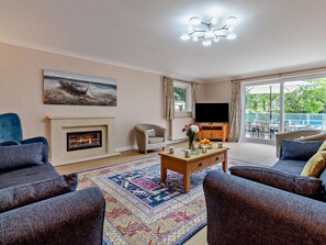 A living room with a fireplace, a television, and a view of the outdoors. - 5 Bed in Woodbridge (oc-72724) (Woodbridge)