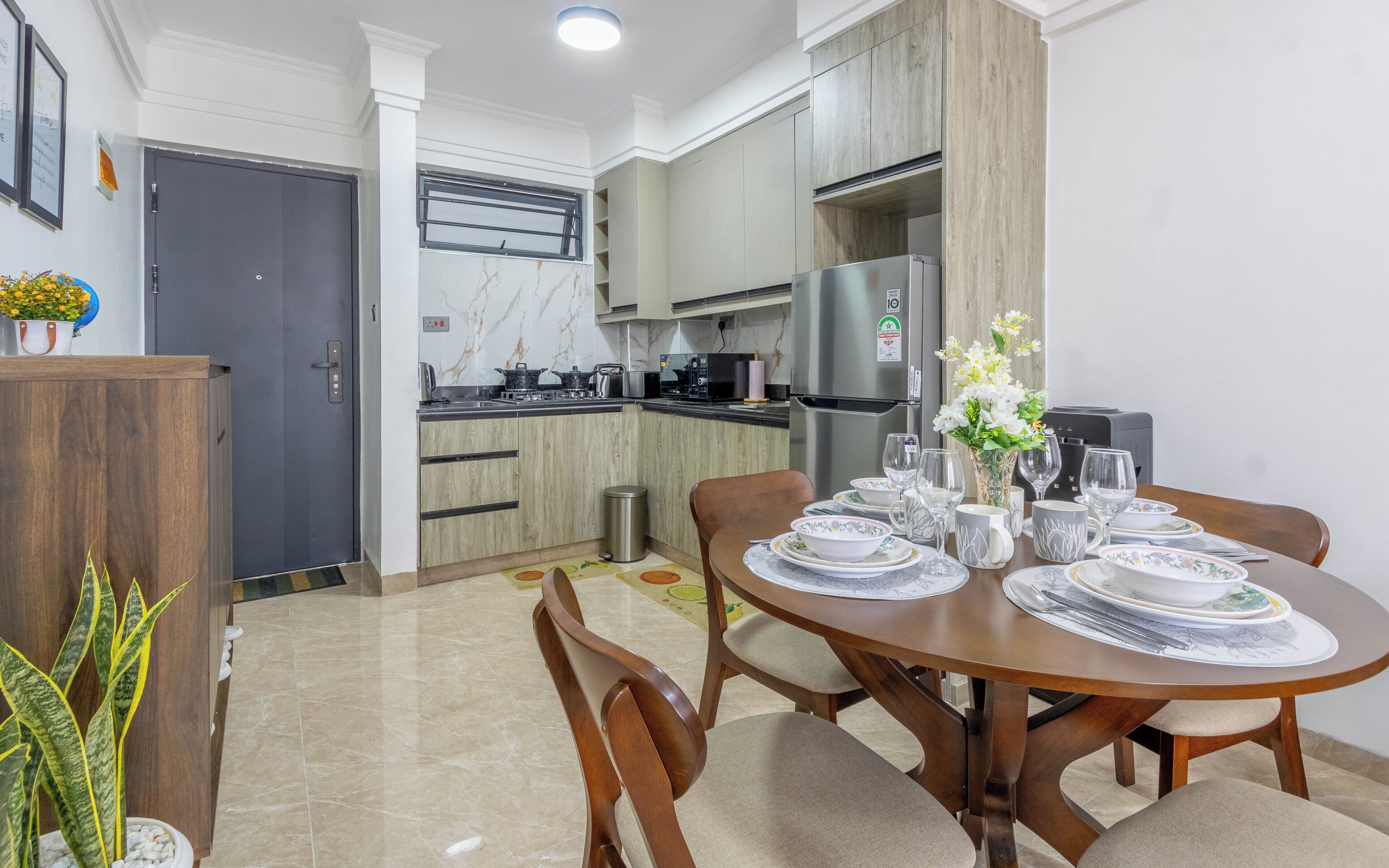 Una cocina moderna con comedor, que incluye una mesa redonda de madera dispuesta para cuatro personas, un refrigerador de acero inoxidable y un salpicadero de mármol.
