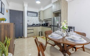 Eine moderne Küche mit Essbereich, inklusive eines runden Holztisches für vier Personen, einem Edelstahlkühlschrank und einer Marmor-Spritzschutzwand.
