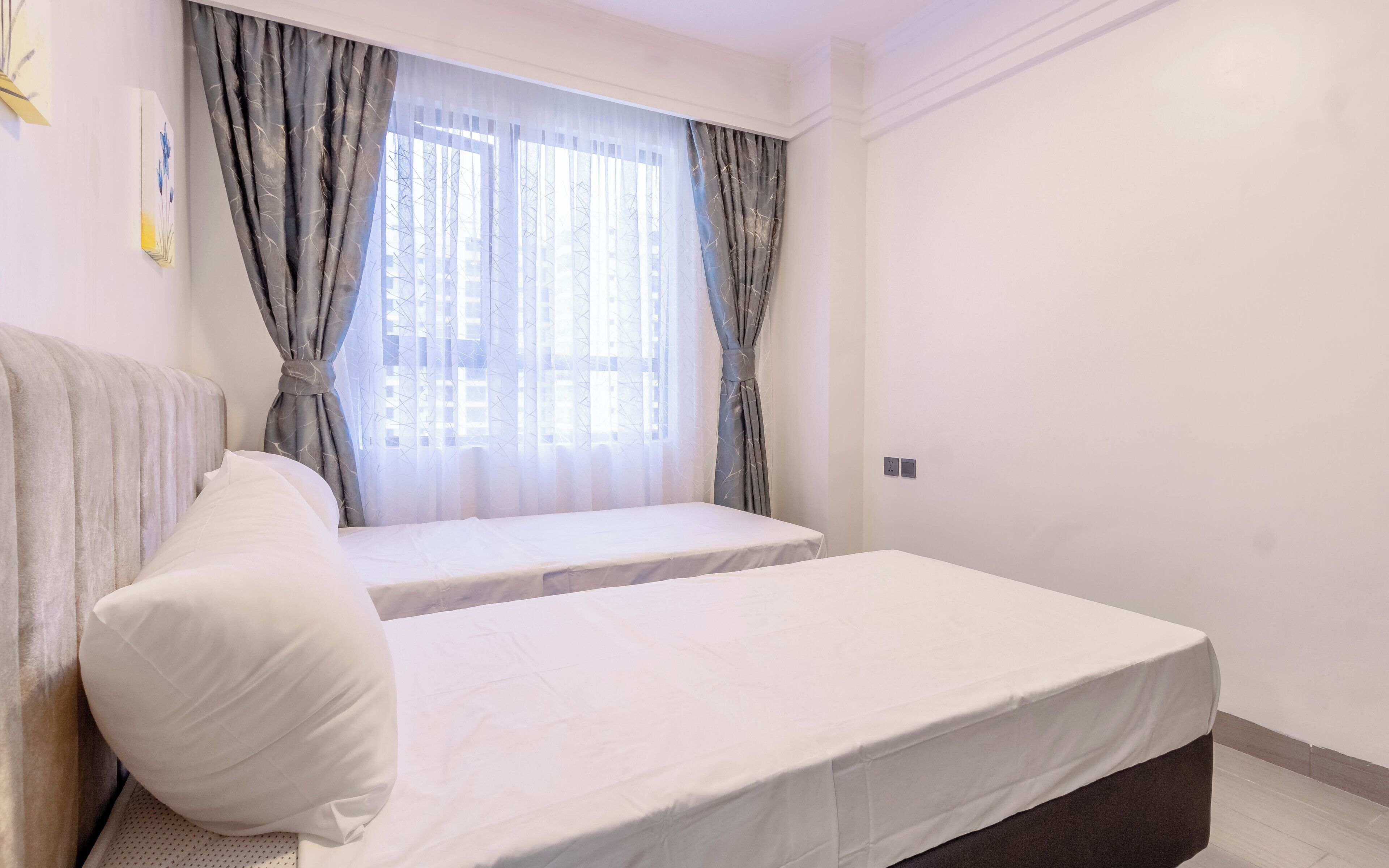 Un dormitorio con cama, almohada, ventana con cortinas y un enchufe en la pared.