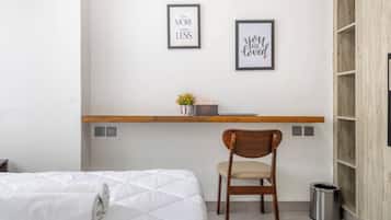 Un dormitorio con cama, una silla, un escritorio con una planta y dos carteles motivacionales en la pared.