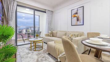 Un salón moderno con sofá, una mesa de comedor, un balcón con vistas a la ciudad y un cuadro en la pared.