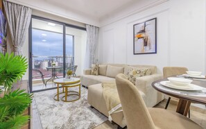 Ein modernes Wohnzimmer mit einer Couch, einem Esstisch, einem Balkon mit Stadtblick und einem Bild an der Wand.