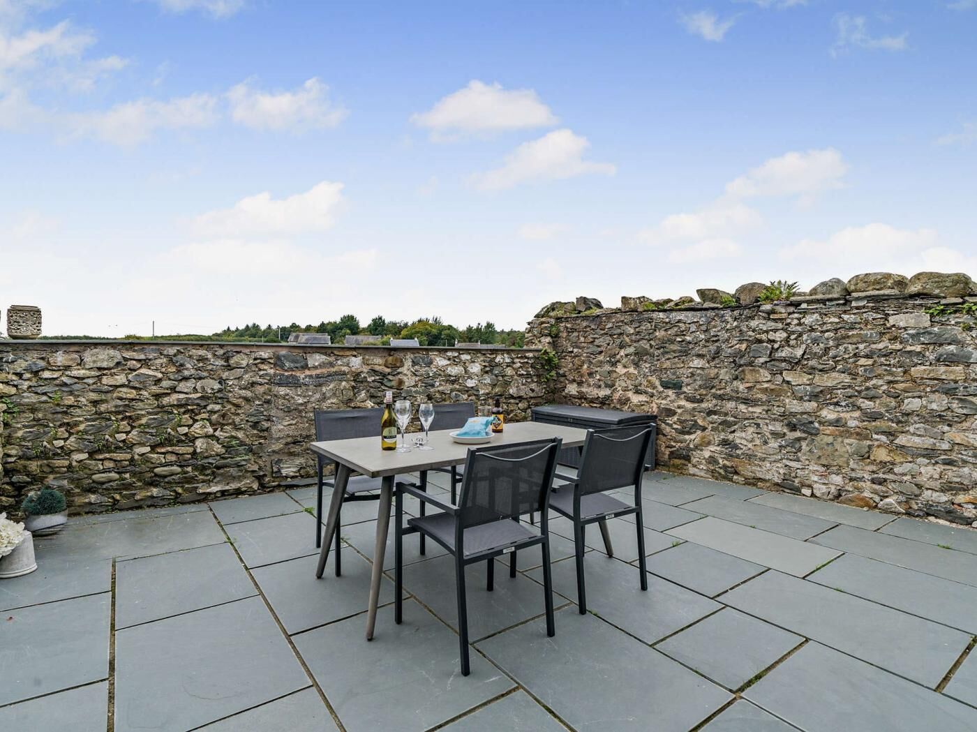 A stone wall, a table with chairs, and a bottle of wine.