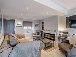 A modern living room with a fireplace, sofas, a coffee table, and a flat-screen TV. - 2 Bed in Grange-over-sands (oc-73154) (Cartmel)