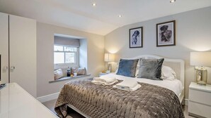 Un dormitorio con cama, mesitas de noche, ventana con vistas y una obra de arte en la pared.