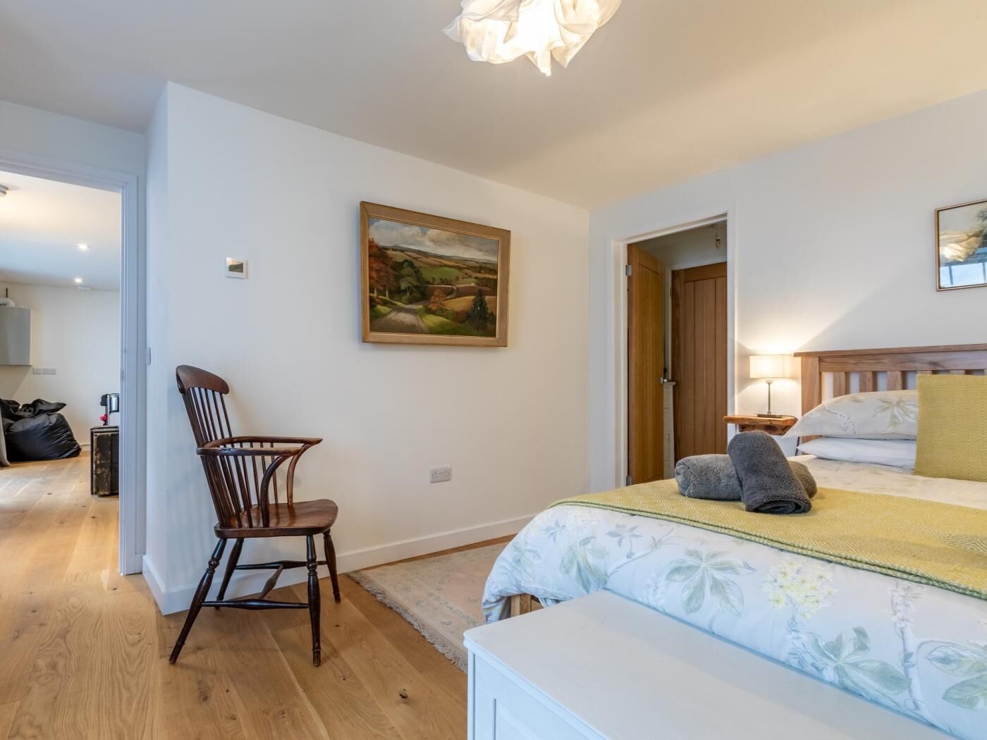 Une chambre à coucher avec un lit, une chaise, un tableau et une porte donnant sur une autre pièce.