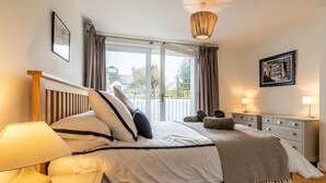 Ein Schlafzimmer mit einem Bett, Nachttischlampen, einem Fenster mit Vorhängen, einer Deckenleuchte und einem gerahmten Bild an der Wand.