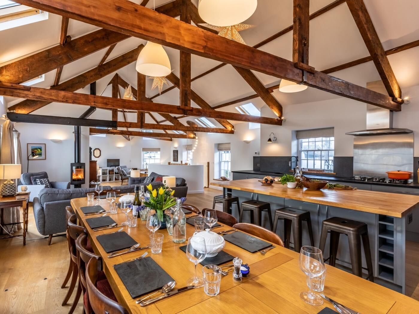 A spacious dining area with a high ceiling and exposed wooden beams, a central island with a stove, and a cozy seating area with a fireplace.