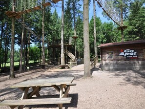 A wooden structure with a picnic table, surrounded by trees and a small building with signage. - 1 Bed in Cinderford (oc-73633) (Ruspidge and Soudley)