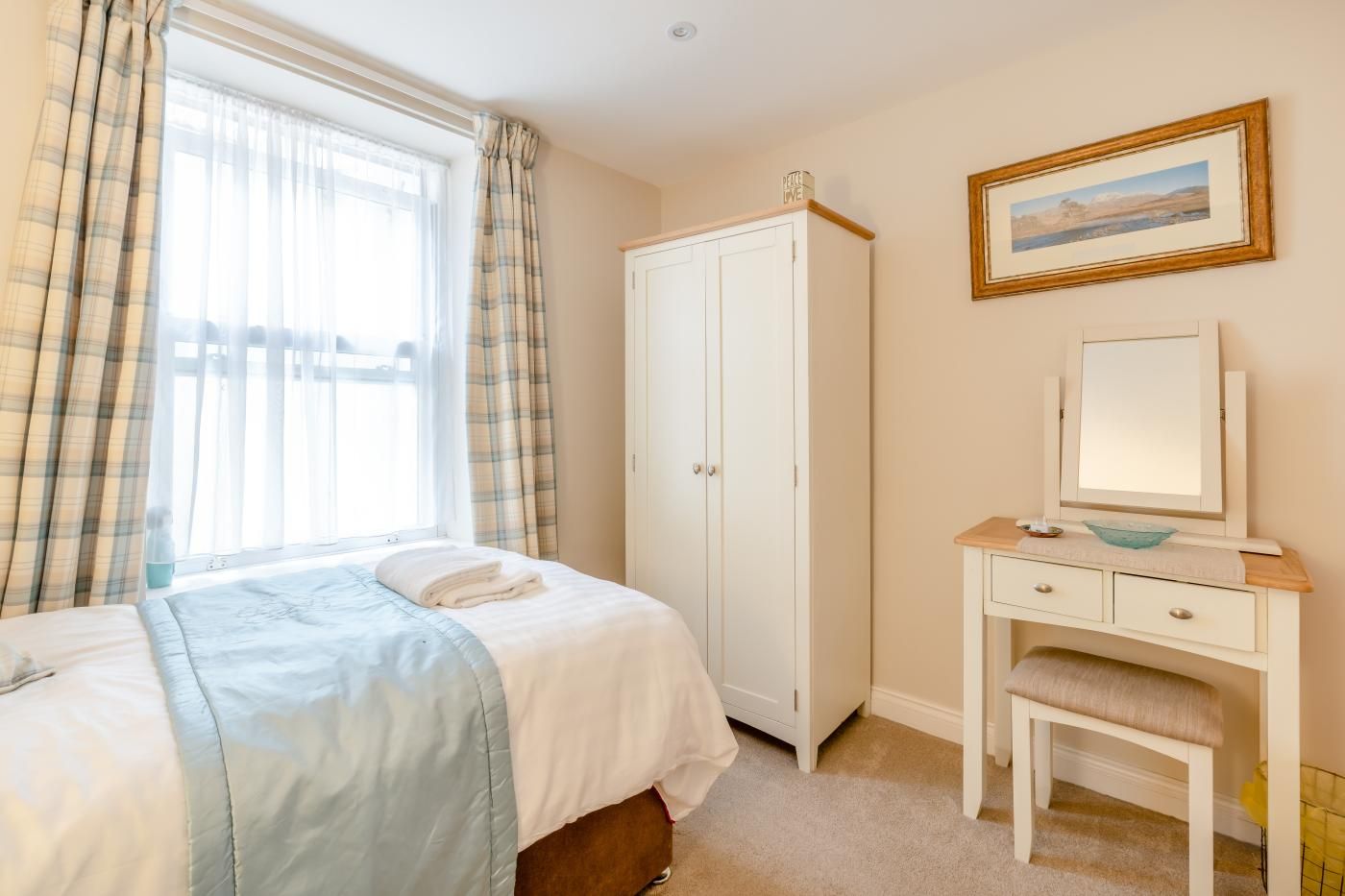 A bedroom with a bed, a wardrobe, a desk with a mirror, and a painting on the wall.