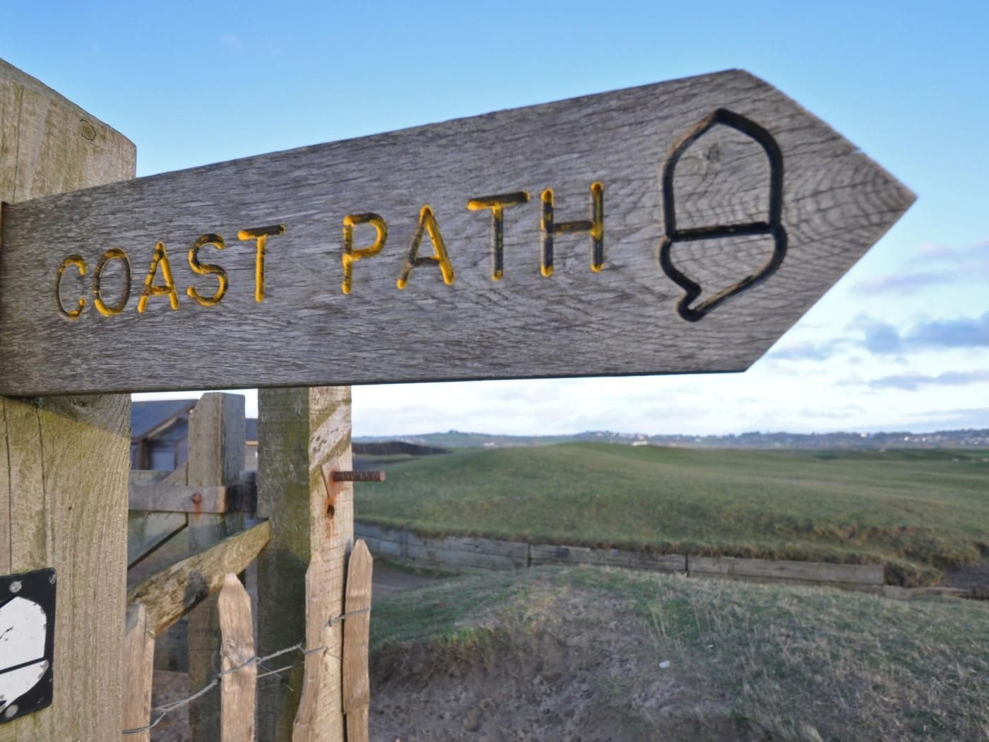 Un panneau indicateur en bois portant l’inscription « SENTIER CÔTIER » et un symbole indiquant la direction de la côte.