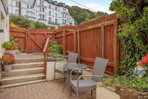 A patio with wicker furniture, a wooden fence, and steps leading to a building. - 2 Bed in Bideford (oc-73895) (Westward Ho!)
