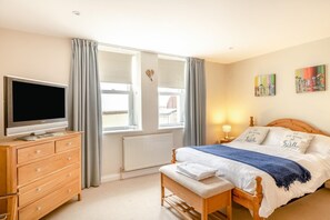 A bedroom with a bed, a TV, a dresser, a window with curtains, and artwork on the wall. - 2 Bed in Bideford (oc-73895) (Westward Ho!)