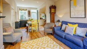 A living room with a blue sofa, patterned armchair, and a dining area with yellow chairs. - 4 Bed in Harrogate (oc-73424) (Harrogate)