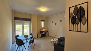 A dining area with a table and chairs, a television on a stand, and a view through a sliding door to the outside. - Estia Chios Apartment B3 (Lefkonia)