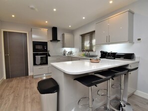 Una cocina moderna con una isla central, taburetes de bar, un microondas y una cafetera.
