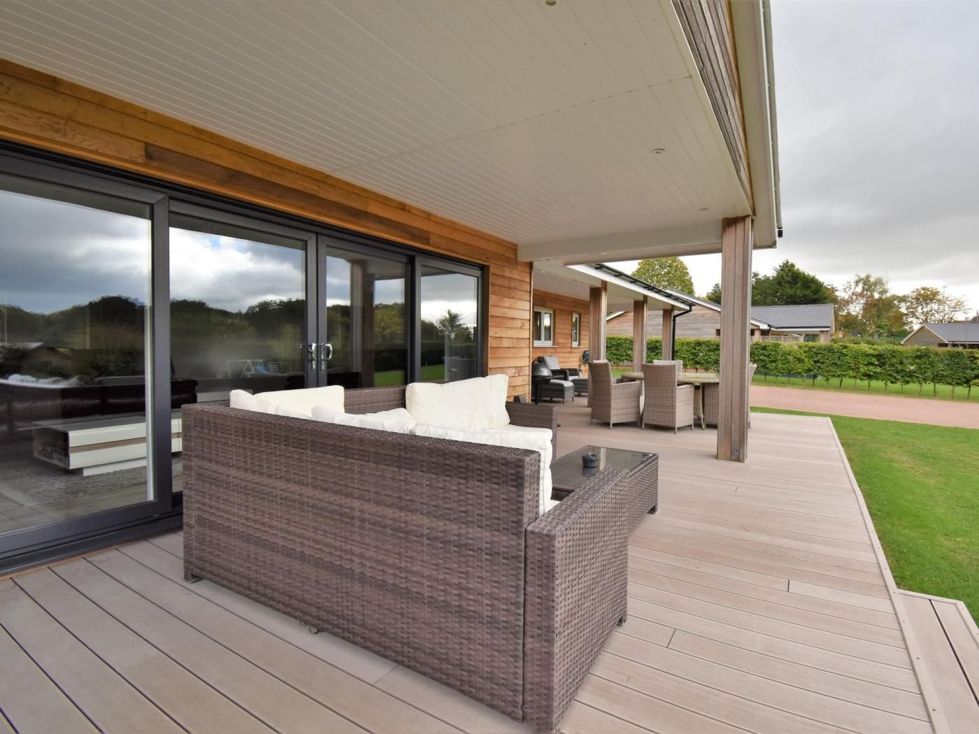 A covered outdoor seating area with a wicker sofa and chairs, a glass door leading to a patio, and a view of the surrounding landscape.