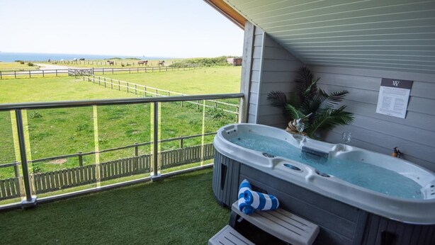 Boblebad på balkon med udsigt til indhegnet græsmark og hav.