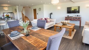 En moderne stue med et træspisebord, grå polstrede stole, en hvid sofa og et tv ophængt på væggen.