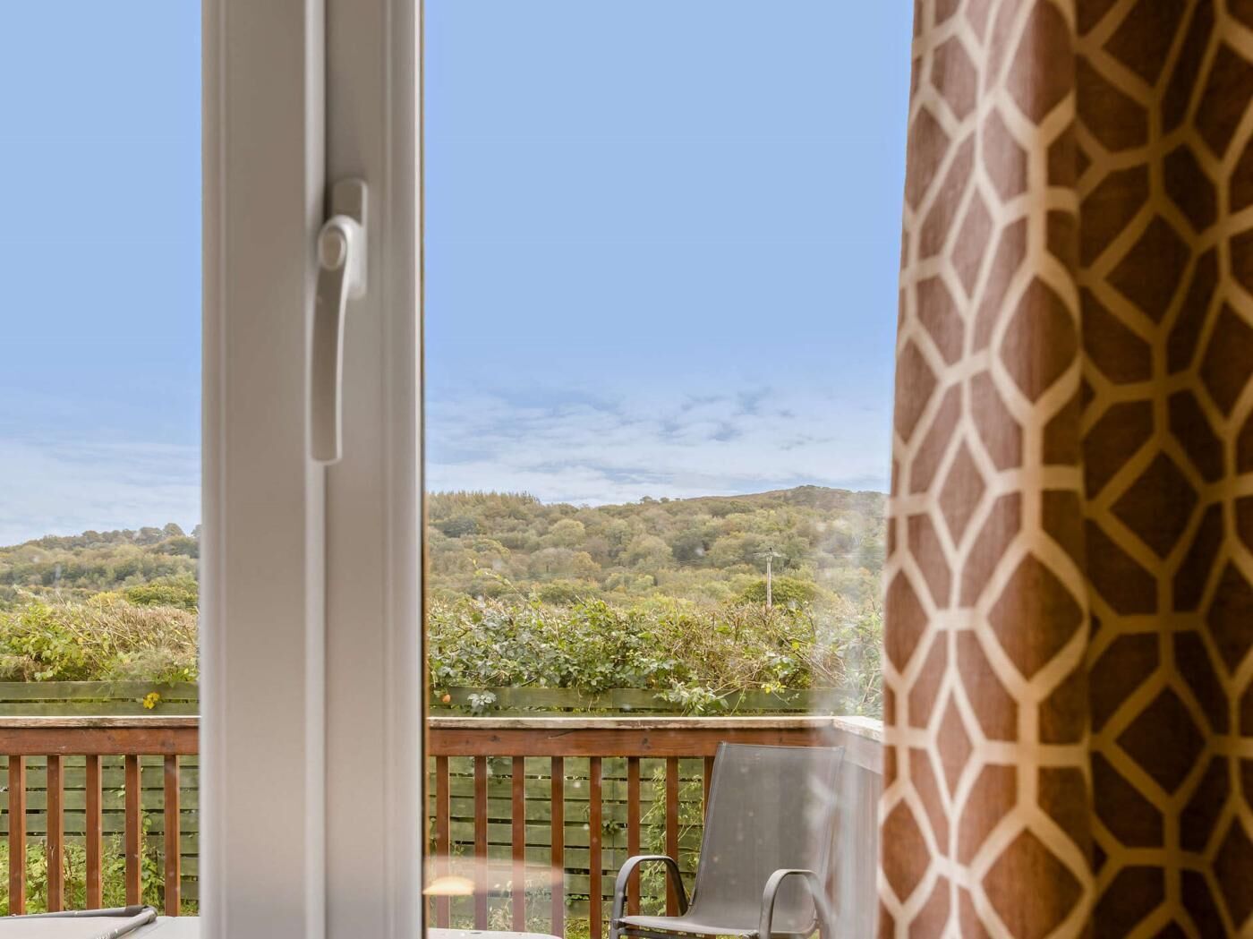 Un balcon donnant sur un paysage boisé, avec une balustrade en bois et une chaise.