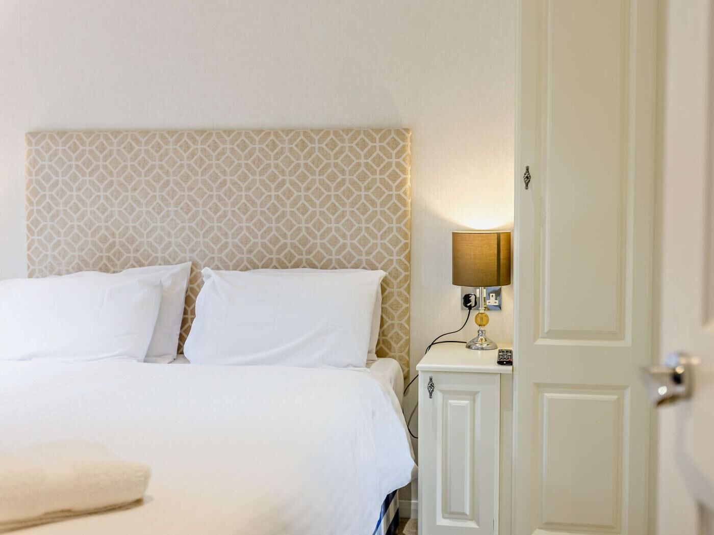 A hotel room with a bed, a bedside lamp, and a door.