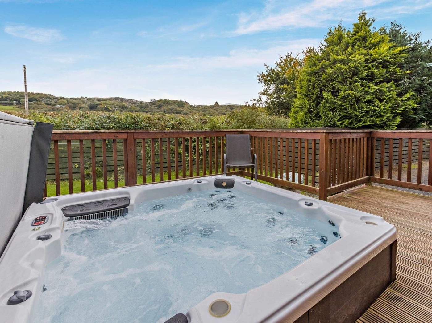 Een hottub op een houten terras, met uitzicht op een groen landschap.