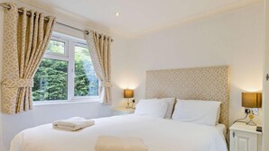 A bedroom with a large bed, two bedside tables with lamps, a window with curtains, and a headboard with a pattern.