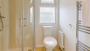 A bathroom with a glass shower enclosure, a toilet, a window with blinds, and a towel rack.