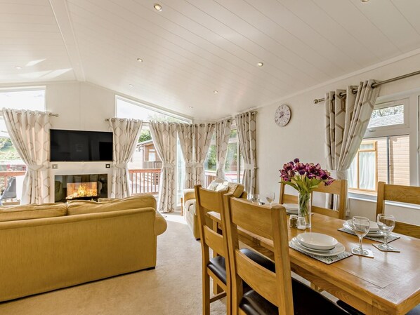A room with a sofa, dining table, chairs, a flat-screen TV, and a fireplace.