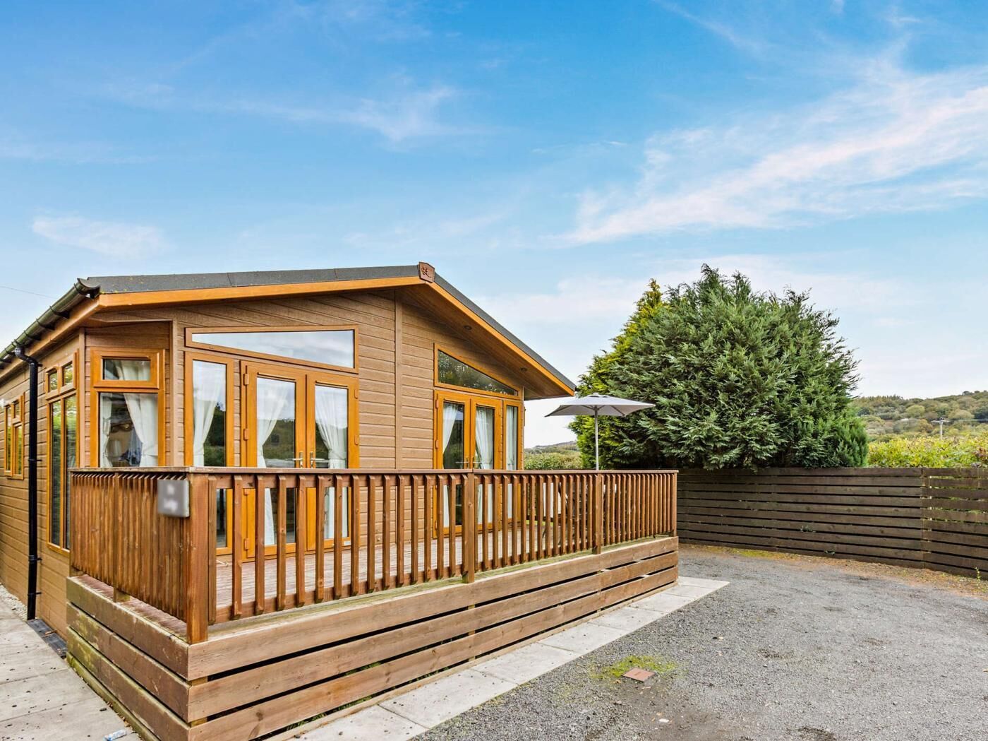 Une cabane en bois dotée de grandes fenêtres, d’un balcon et offrant une vue sur un arbre et des collines.