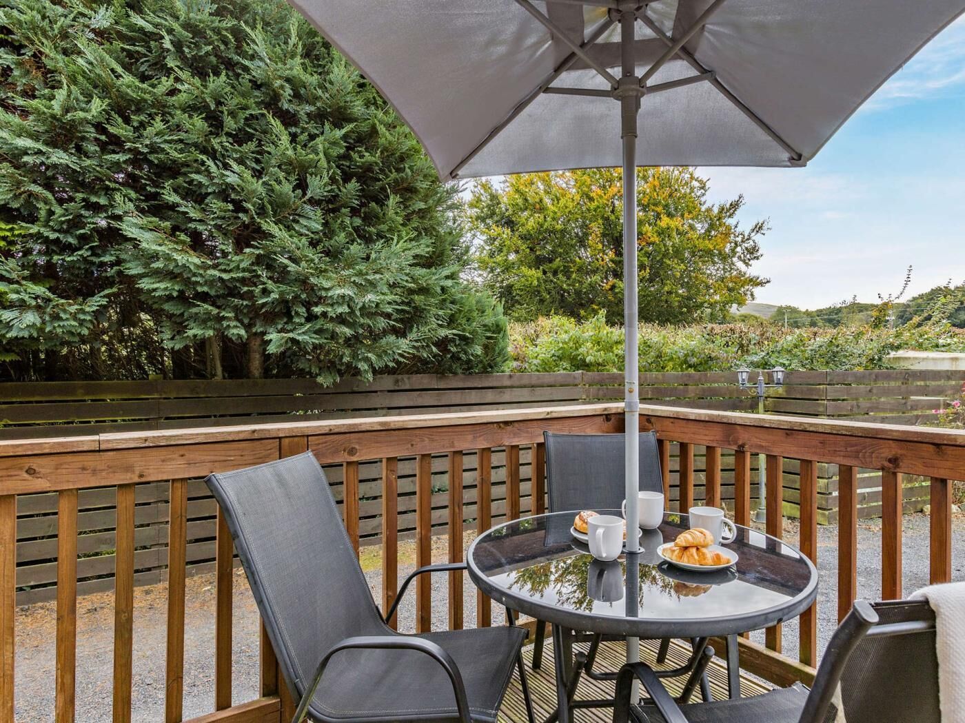 A wooden deck with a round glass table, two chairs, and an umbrella.